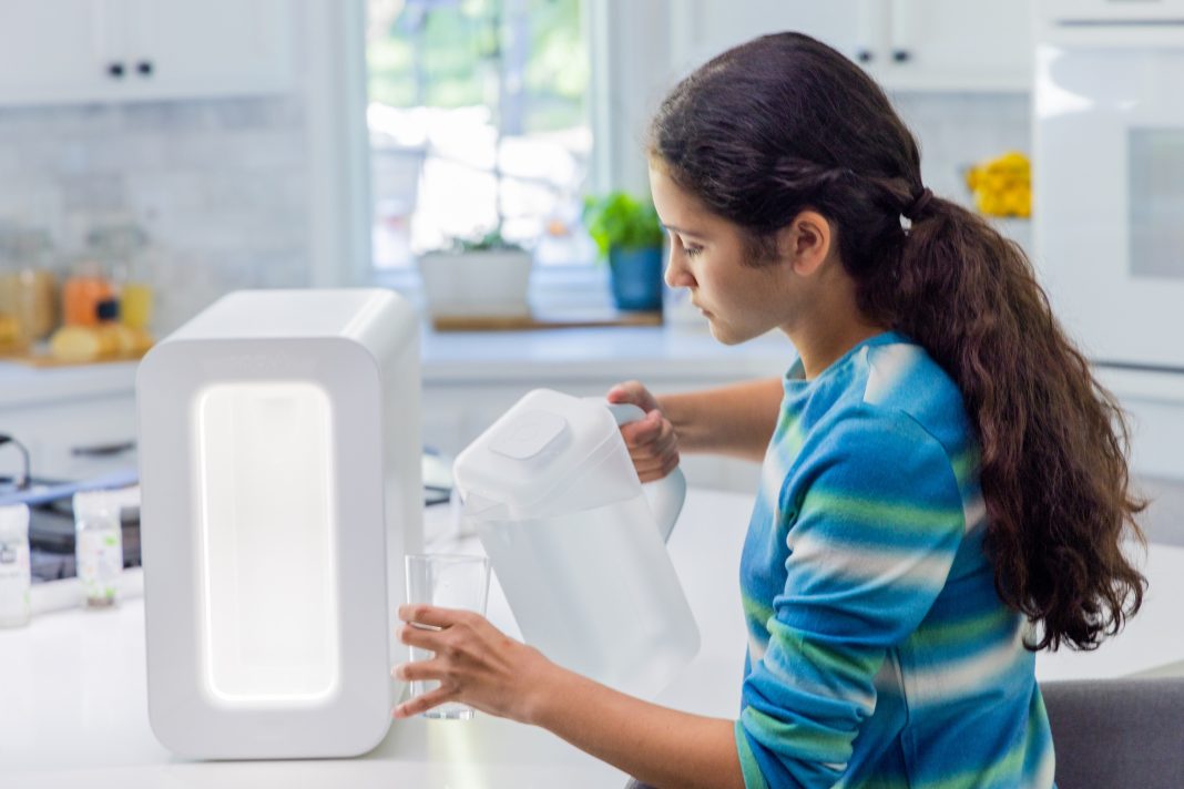 girl pouring water from spout atmospheric water generator into a drinking glass