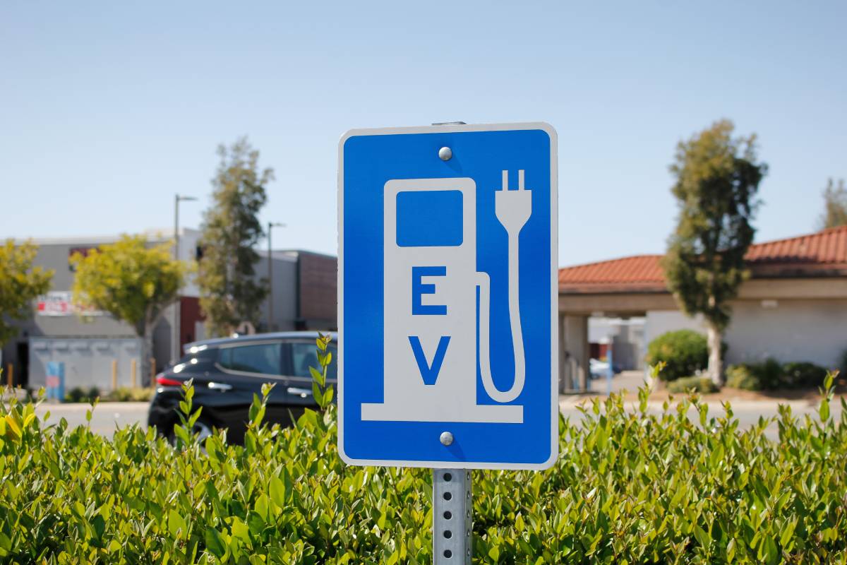 A blue and white sign signifying a charging station in a parking lot shows a cartoon "pump" with the initials "EV."
