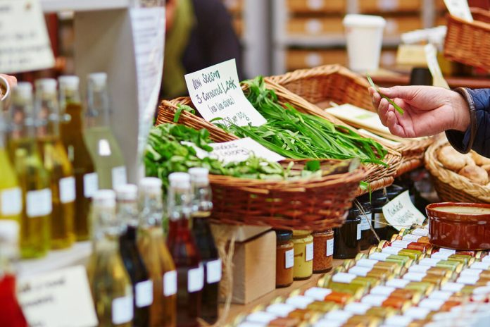 A person examining leeks for sale at a farmers market booth. There are also mushrooms and oils at the booth.