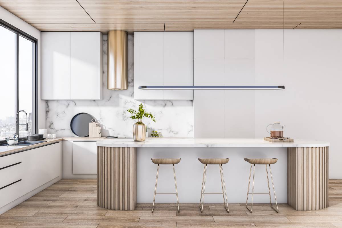 A modern kitchen with brown flooring, a white island with brown stools, white cabinets, and large window above the sink.