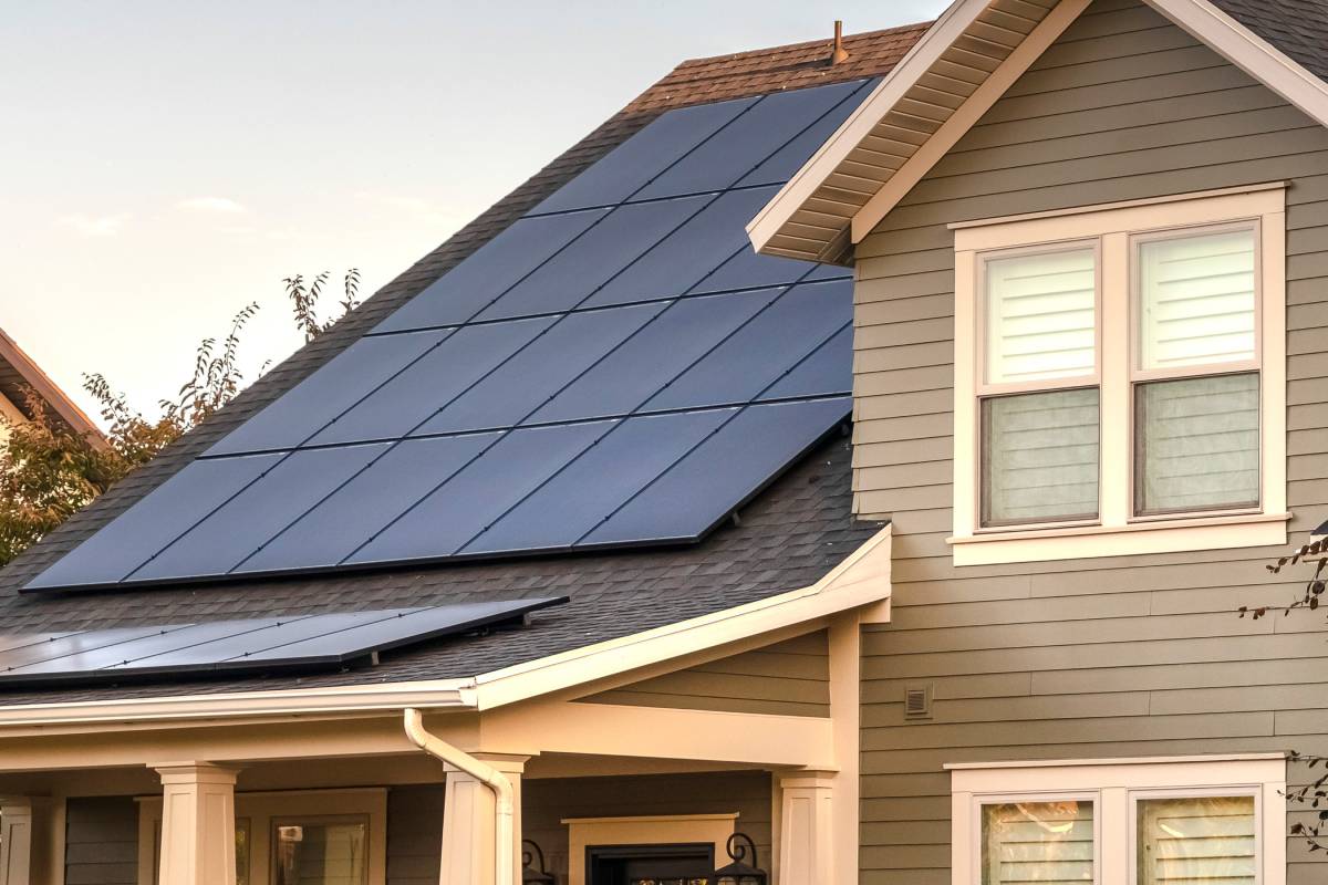 A residential home with solar panels installed on the roof. The roof is a steep slant with solar panels facing the sky.