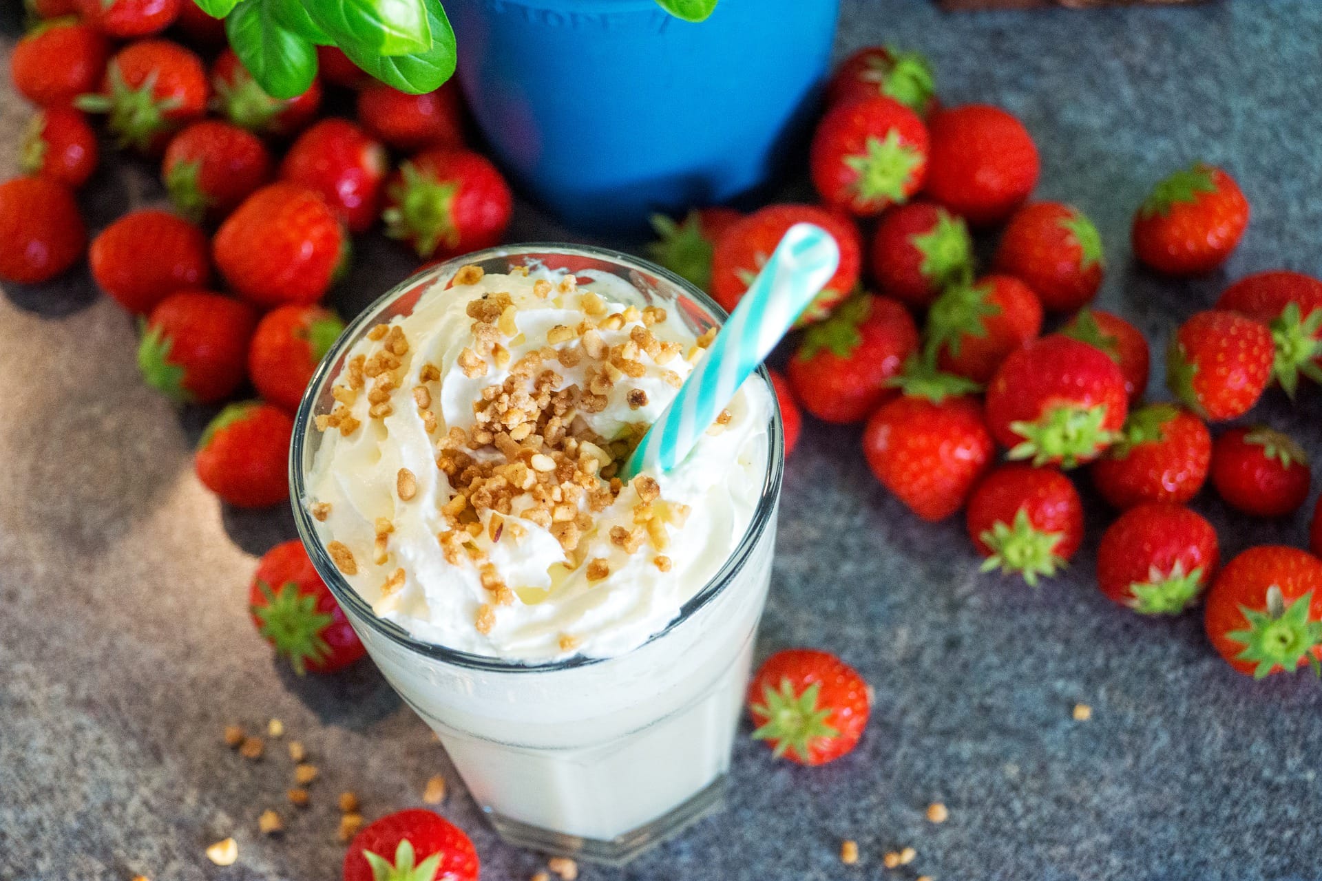 Protein shake in a glass with a straw surrounded by strawberries