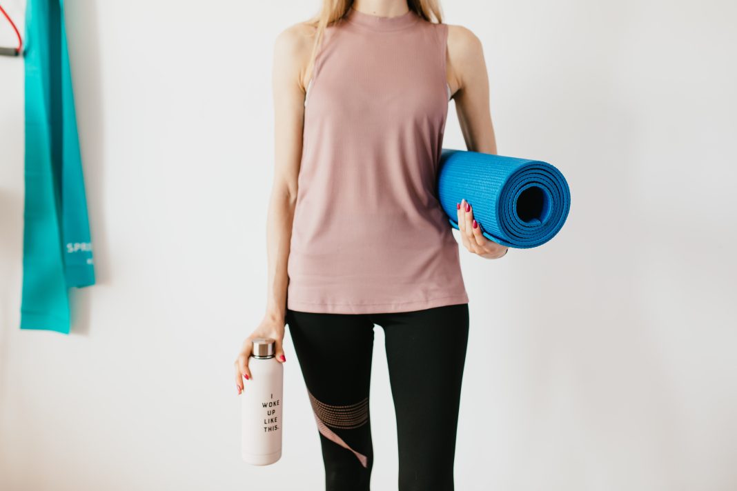 woman holding stainless steel water bottle and yoga mat