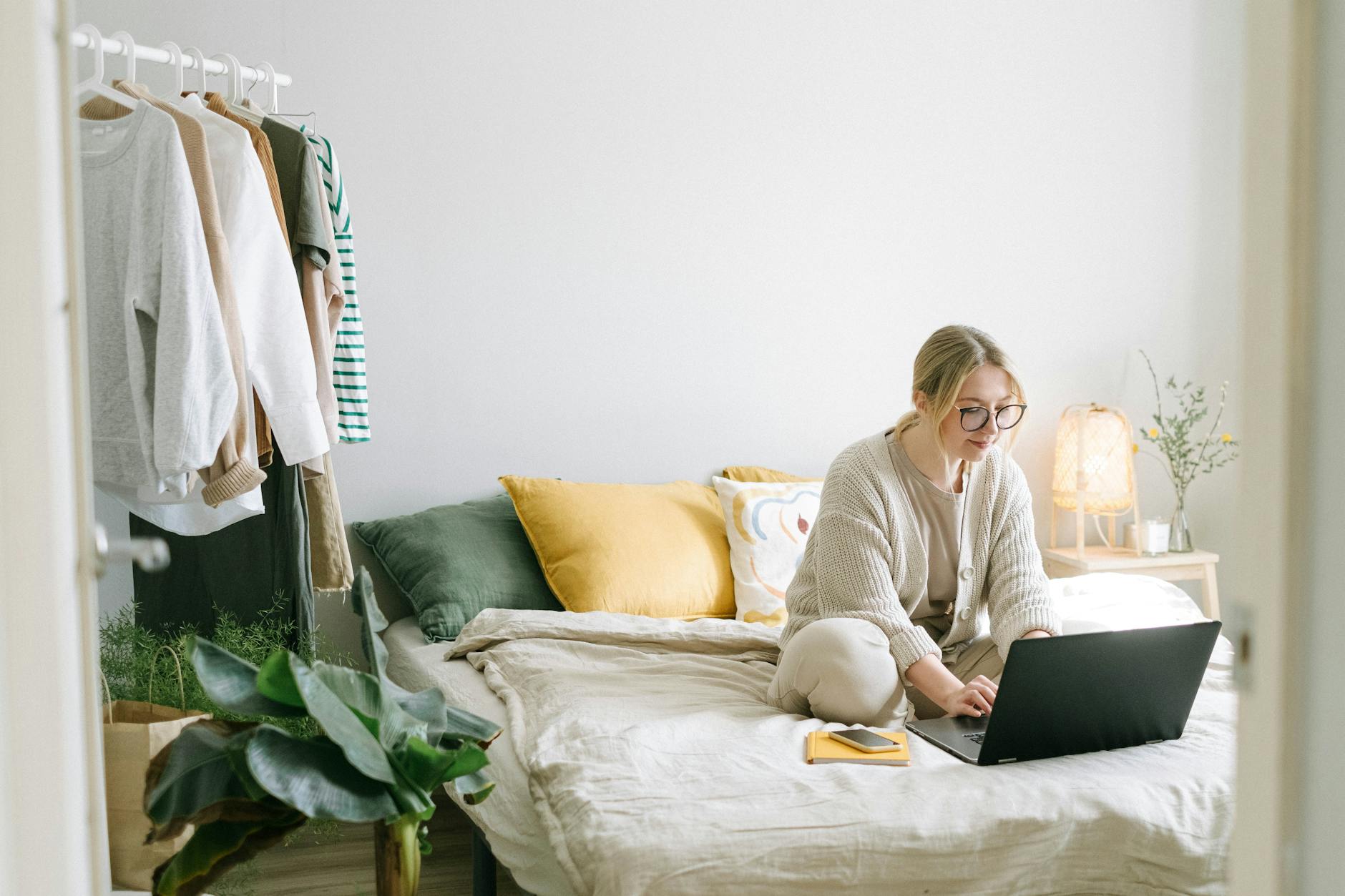 a woman sitting on the bed while using a laptop