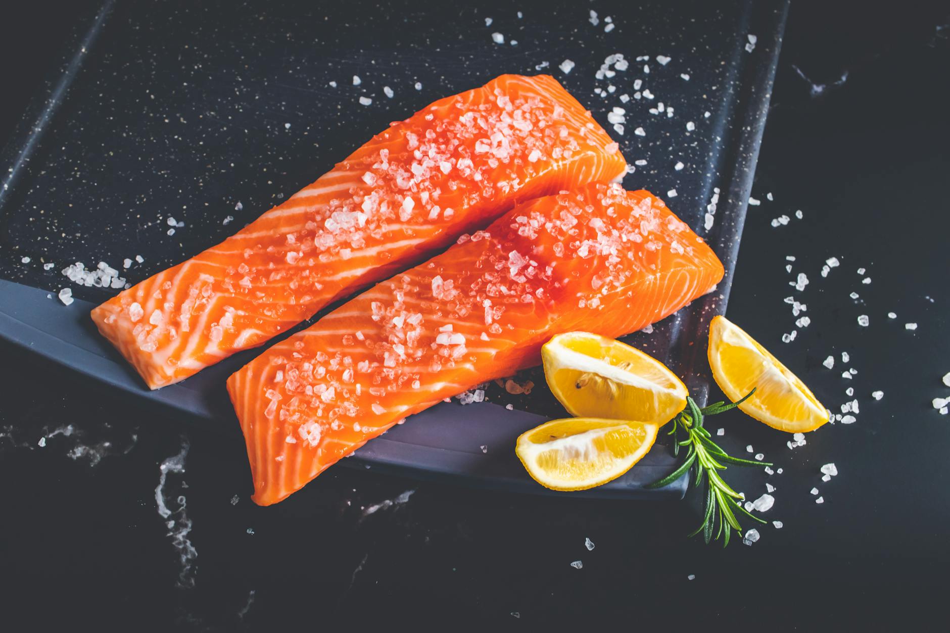 raw pieces of salmon with salt and lemon wedges on a baking tray