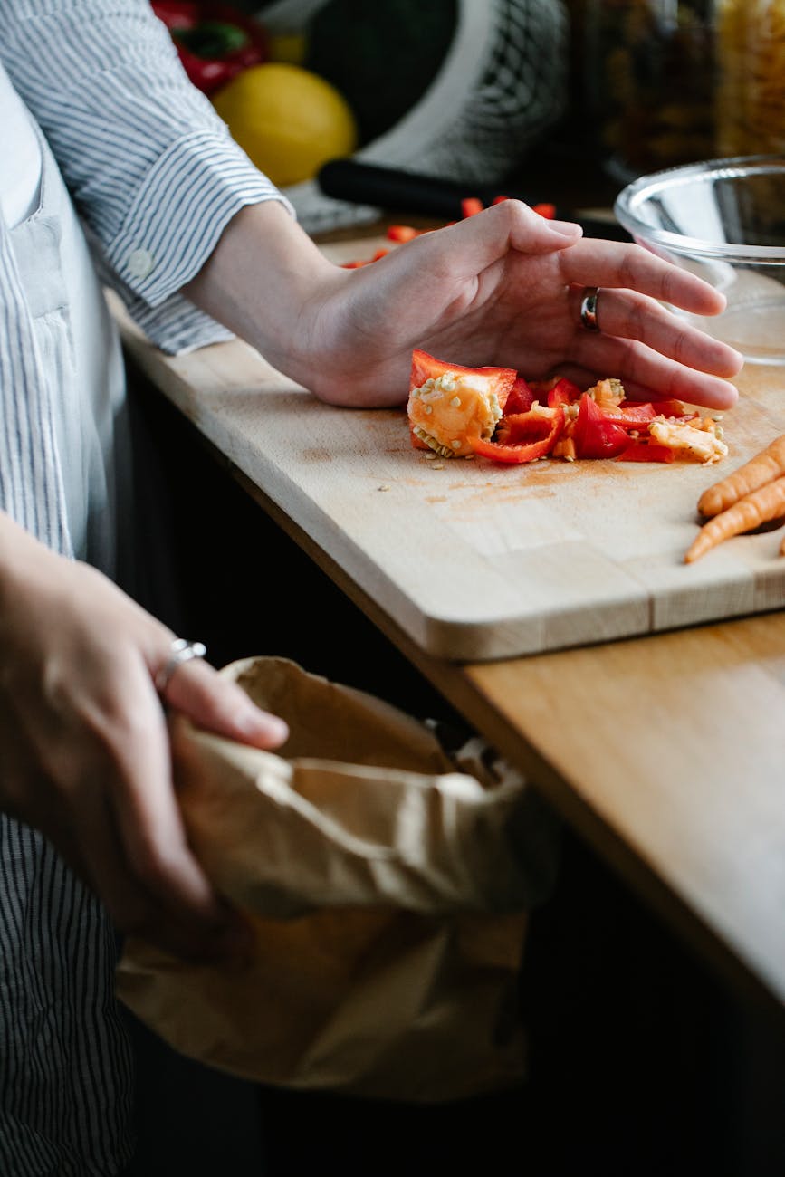 crop unrecognizable housewife throwing waste while cooking in kitchen