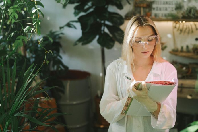 focused woman in white lab coat writing down on a notebook