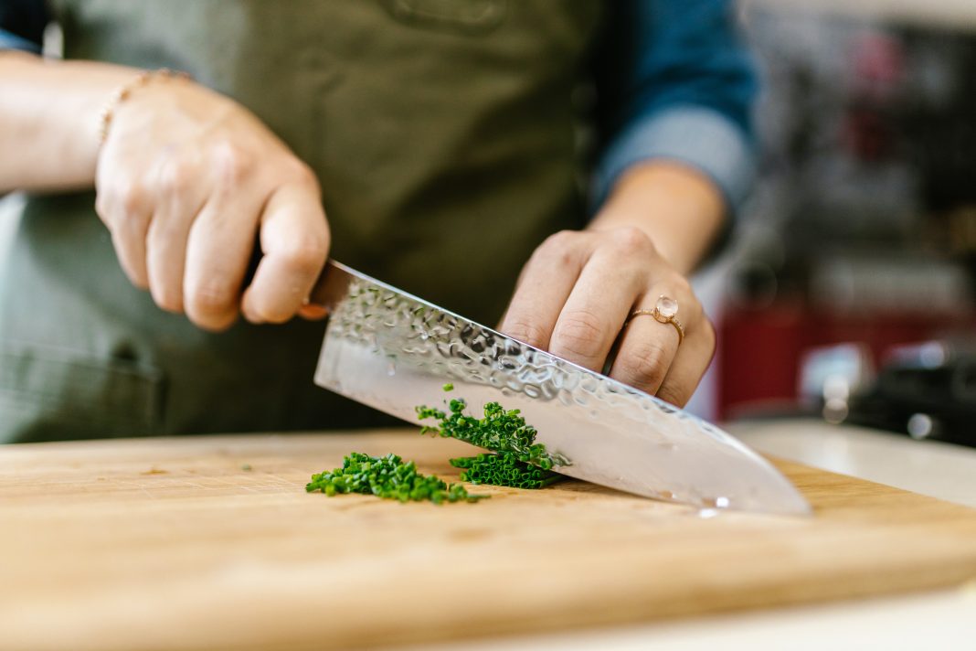 person cutting green herbs on a bamboo cutting board